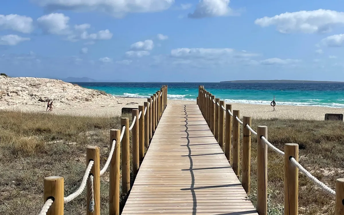 A wooden boardwalk with rope rails running through the dunes to turquoise water