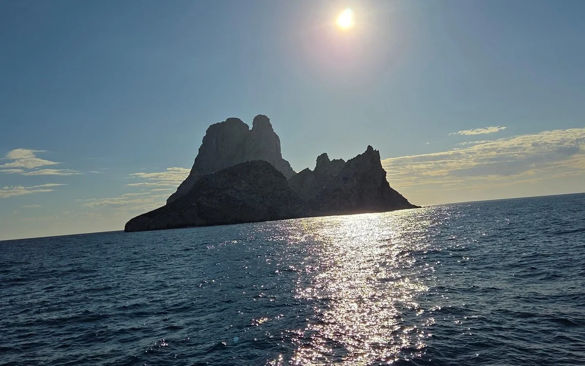 The rock island of Es Vedr&agrave; in silhouette against the sun over the sea