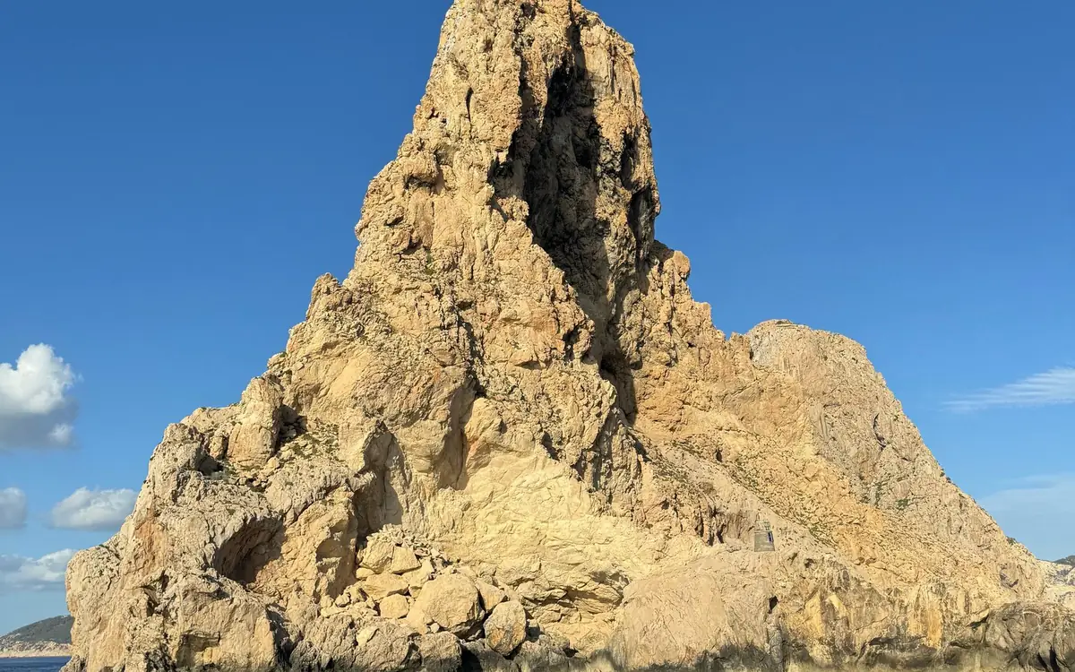 Sheer golden limestone of the Es Vedrà reserve rising against a deep blue sky