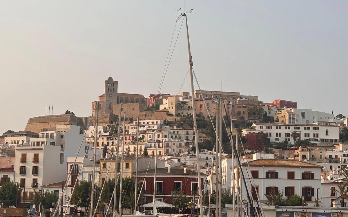 Sailing masts in Ibiza harbour below the walled upper town and its cathedral tower