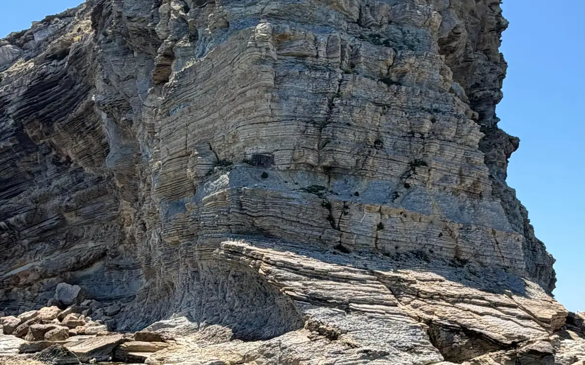 A sea cliff of layered pale limestone under a clear blue sky