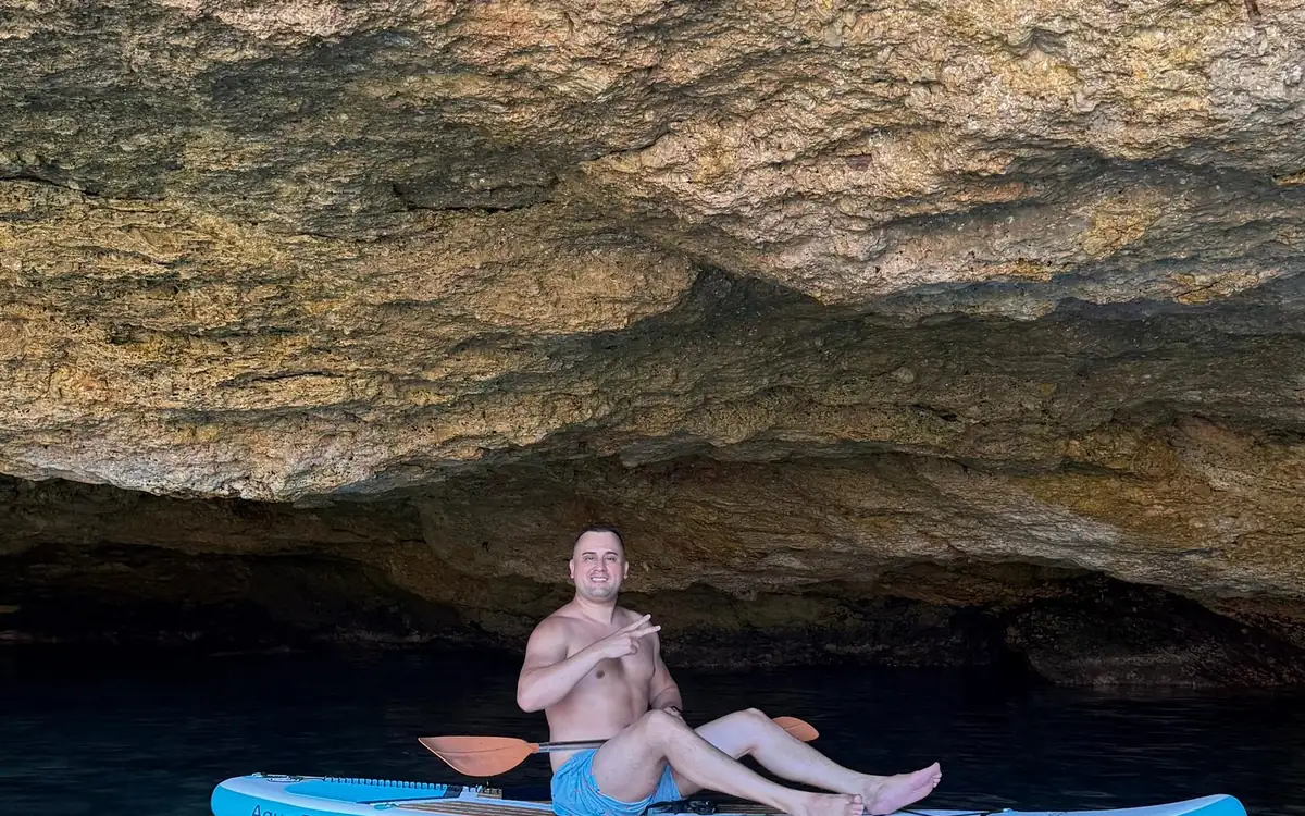 A man sitting on a paddle board under the low rock roof of a sea cave