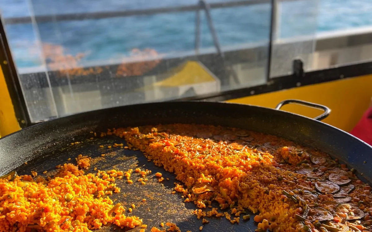 Paella cooking in a wide pan on the deck of a boat