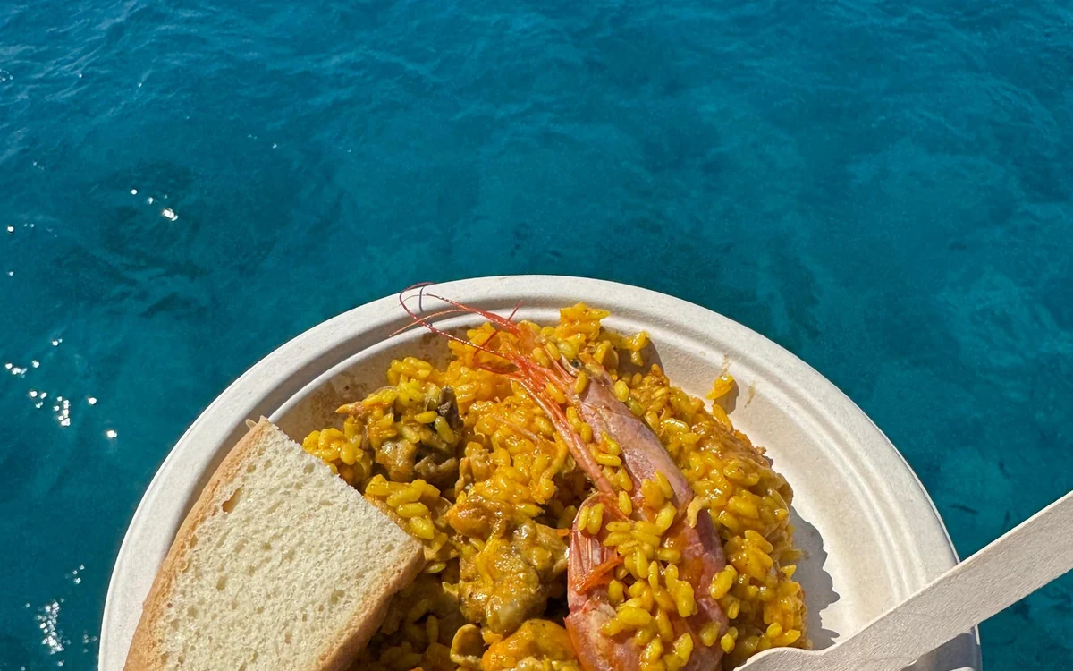 A plate of paella with a prawn and a slice of bread, deep blue water below