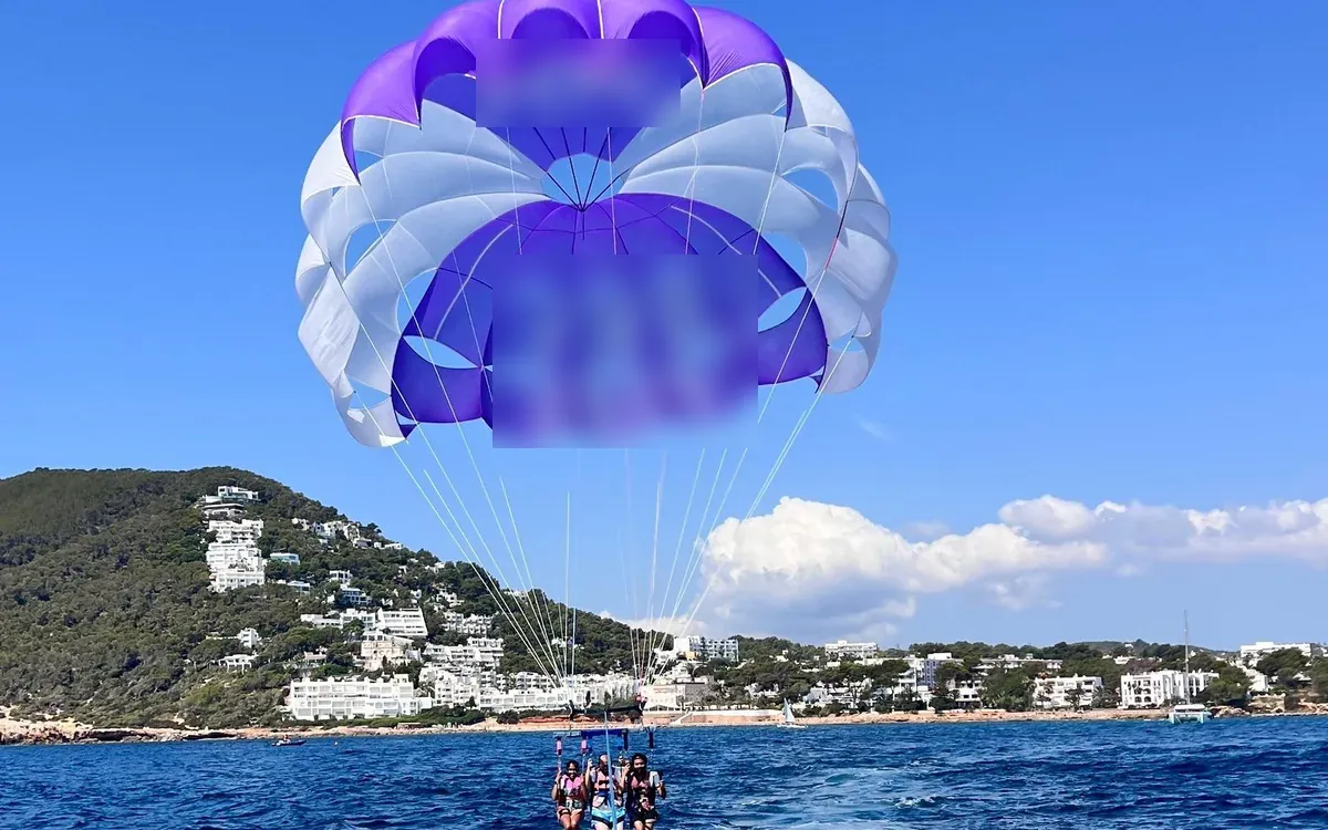 A purple parasail in the sky above a boat off a wooded coast