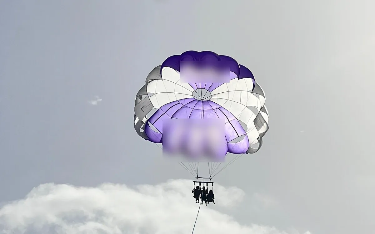Three riders hanging under a purple and white parasailing canopy, a bank of white cloud below