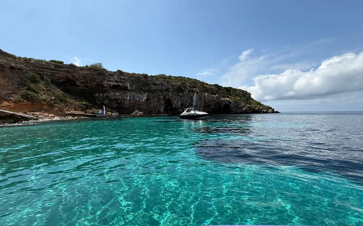 A motorboat in a turquoise cove below low rocky cliffs