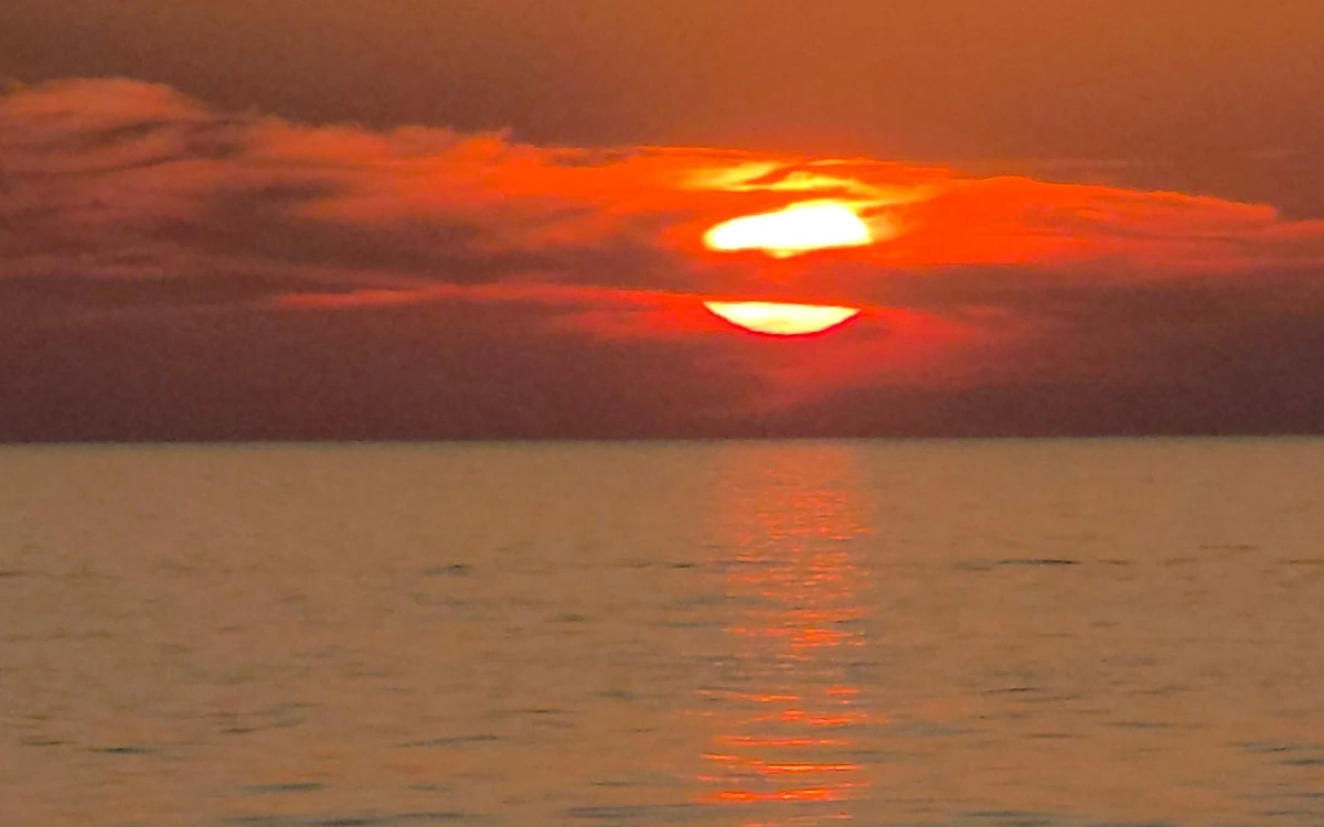 The sun half hidden by red cloud low over the sea, its light on the water