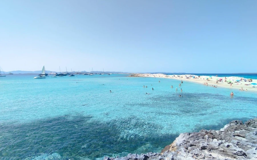 A long white sand spit beside shallow turquoise water, boats anchored offshore