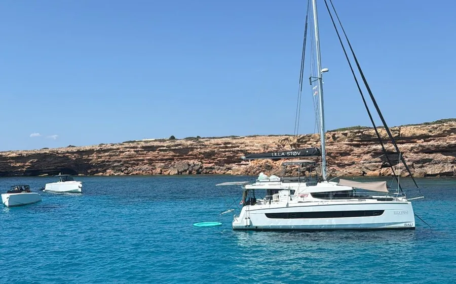 A white catamaran anchored below low rocky cliffs, small boats nearby