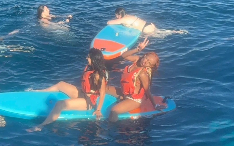 Guests in life jackets sitting on paddle boards in open water, swimmers alongside