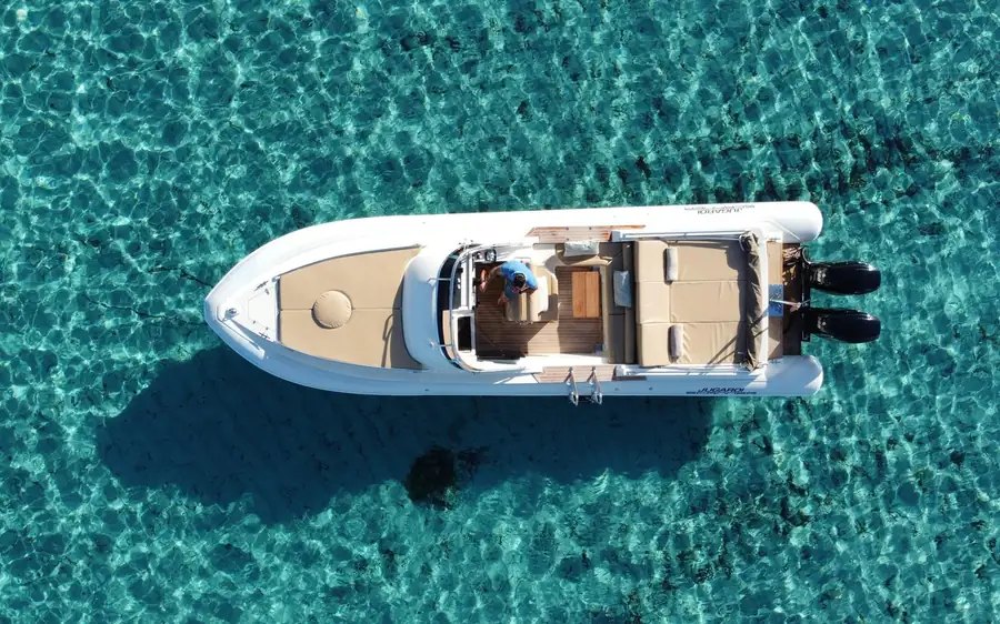 A white rigid inflatable boat on clear turquoise water, seen from above