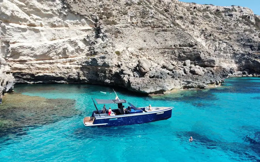 A dark blue motorboat in a turquoise cove below pale limestone cliffs