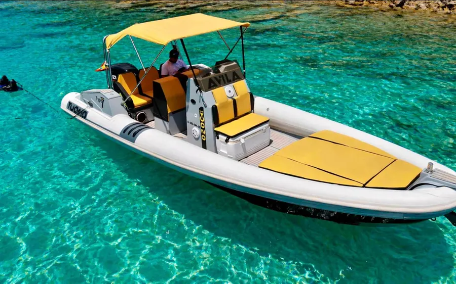 A small rigid inflatable boat with yellow cushions and a sun canopy in a turquoise cove