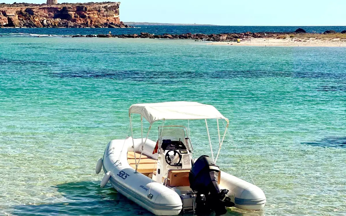 A small inflatable boat with a sun canopy in clear turquoise shallows off a beach