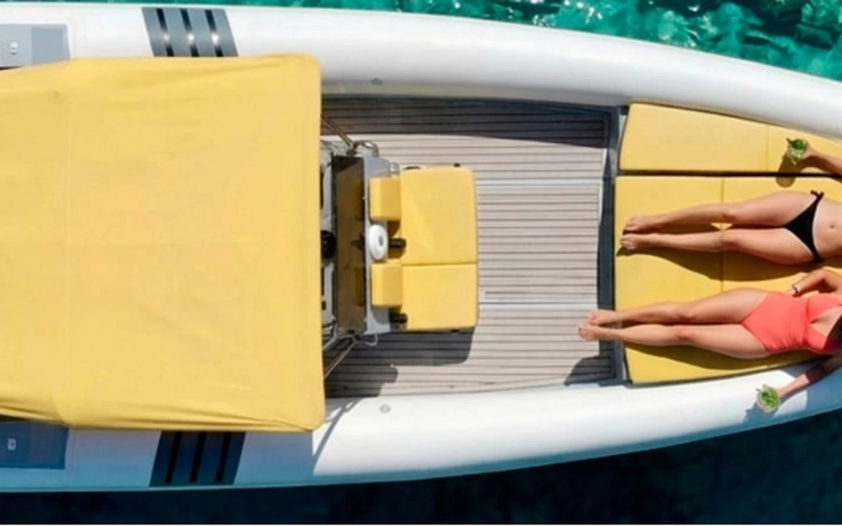 Two people sunbathing on yellow cushions at the back of a boat, seen from above